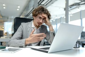 Frustrated young businessman with curly hair facing challenges at work in office